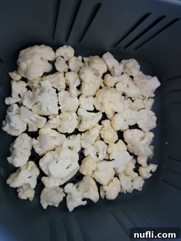 Freshly cut cauliflower florets, glistening with olive oil and spices, arranged in a single layer within an air fryer basket, ready for cooking.