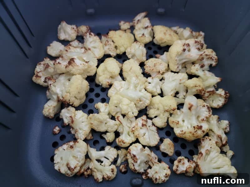 Crispy, golden-brown air-fried cauliflower florets scattered inside an air fryer basket, ready to be served or tossed.