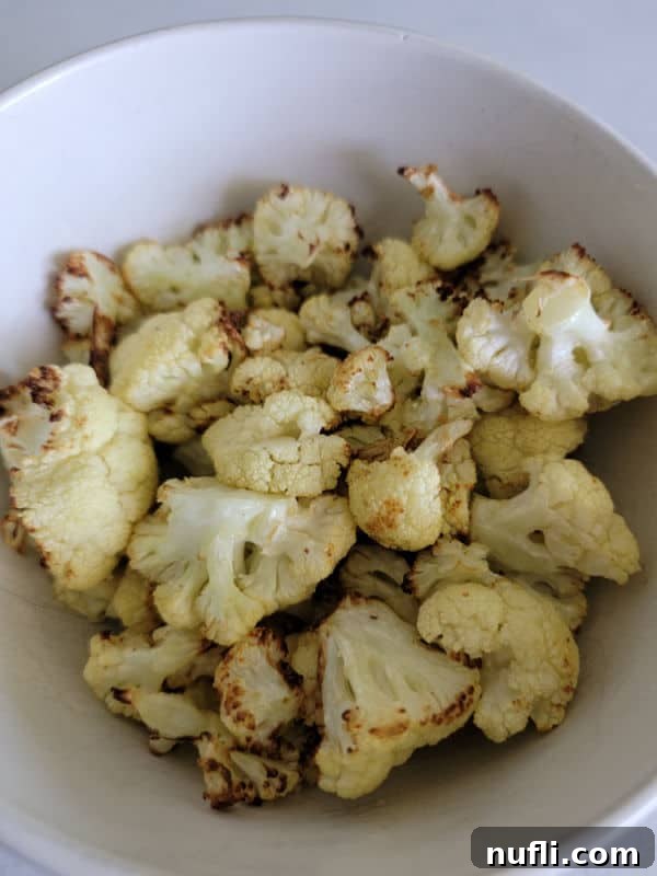 A vibrant white bowl filled to the brim with golden, crispy air-fried cauliflower florets, ready for serving.