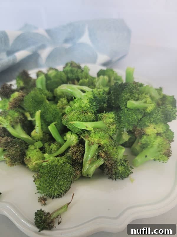 Air fried broccoli on a white plate next to a cloth napkin