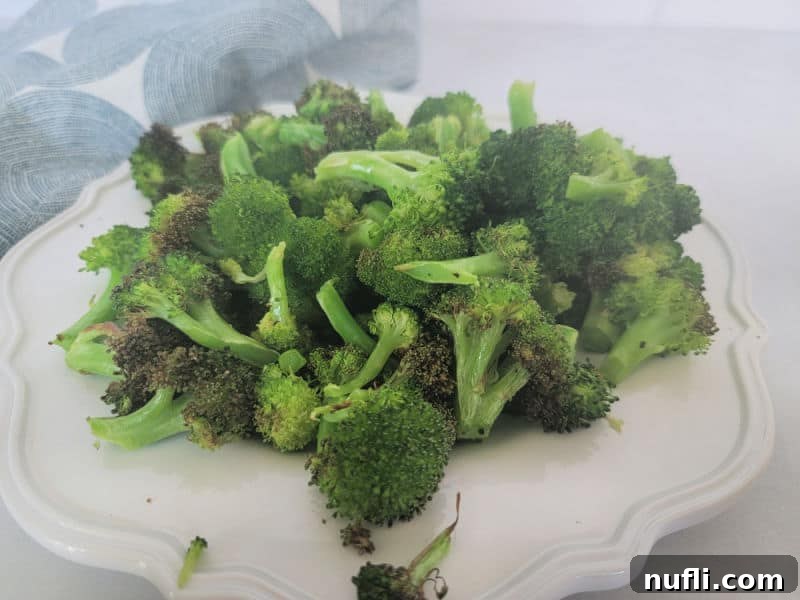 Air fried broccoli on a white plate next to a cloth napkin