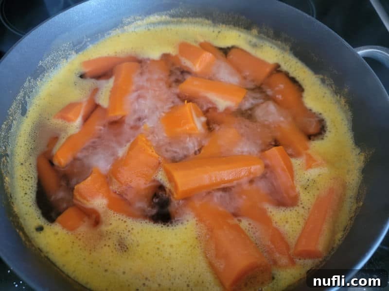 Easy Fluffy Carrot Soufflé 4 Fresh carrots boiling in a dark saucepan on a stovetop, softened and ready for the next step of making carrot soufflé