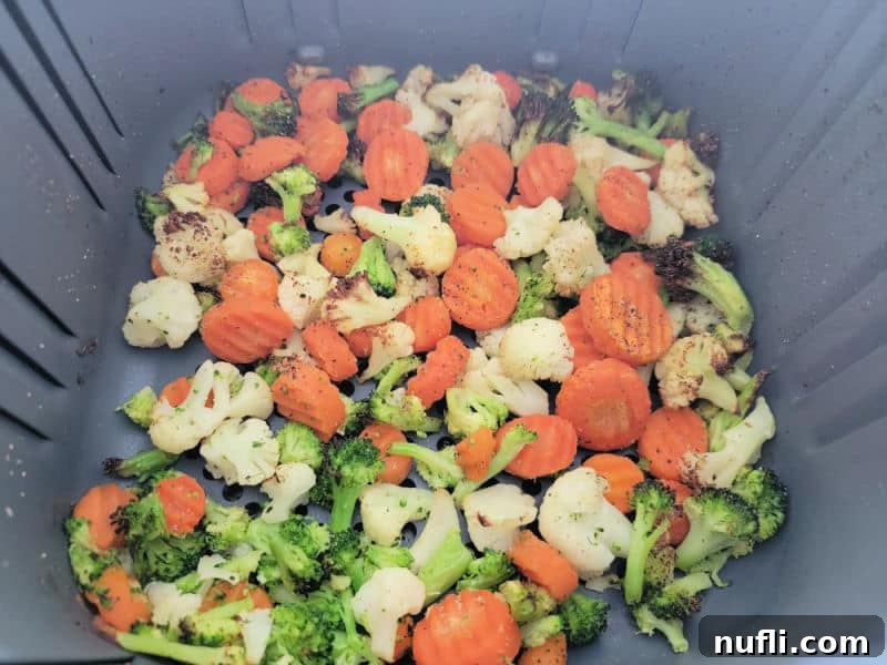 Perfectly cooked mixed vegetables in an air fryer basket, showing a crispy texture.
