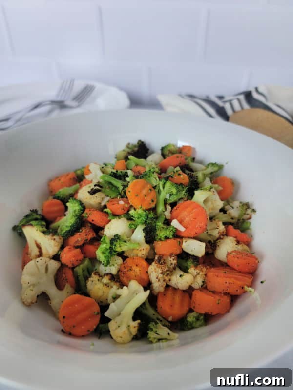 Air fried broccoli, carrots, and cauliflower served on a white plate with a wooden spoon and cloth napkin.