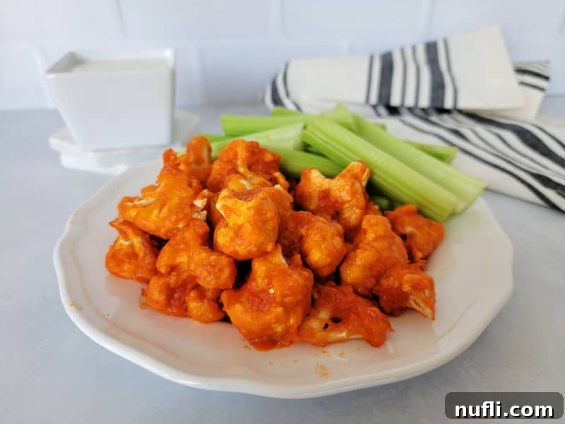 Air fried buffalo cauliflower on a white plate with celery sticks next to a napkin