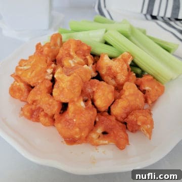 Air Fryer buffalo cauliflower on a white plate with celery next to a cloth napkin