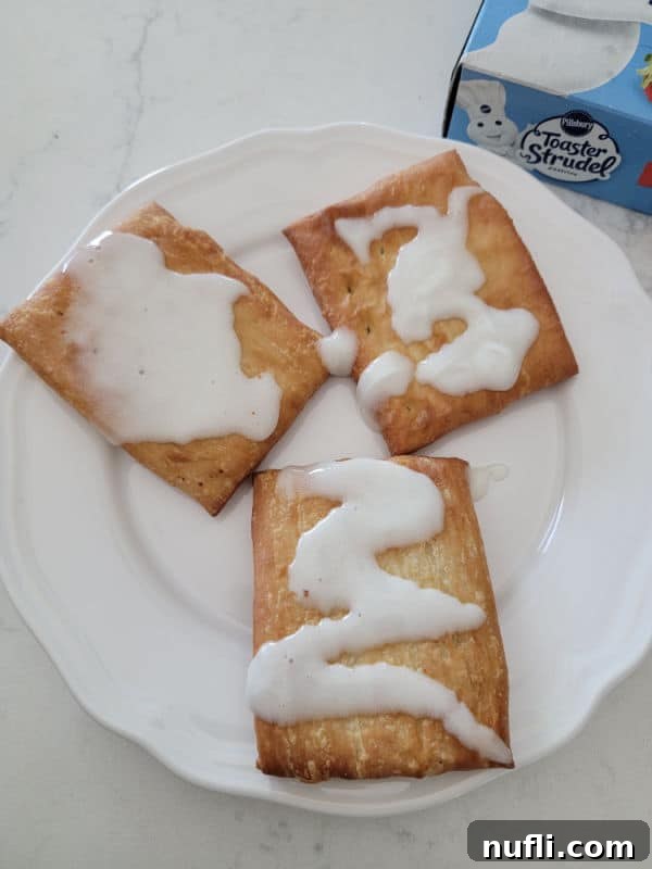 Golden Air Fryer Toaster Strudels 6 Air fried toaster strudel with a generous drizzle of icing on a white plate.