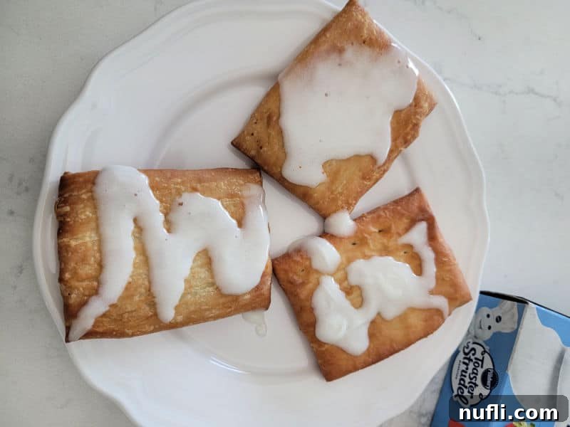 Golden Air Fryer Toaster Strudels 7 A freshly air fried toaster strudel on a white plate, with an open box of frozen toaster strudels in the background.