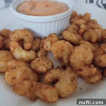 Crispy Air Fryer Frozen Popcorn Shrimp 6 air fried shrimp on a white plate next to a bowl of sauce