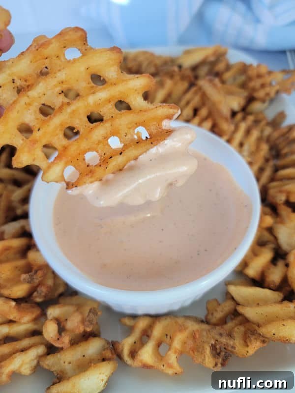 Waffle fry dipping into Comeback sauce in a white bowl surrounded by fries