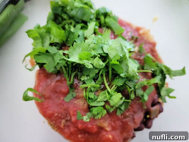 Freshly chopped cilantro ready to be added to a bowl of salsa and other ingredients, highlighting the vibrant green and red colors.