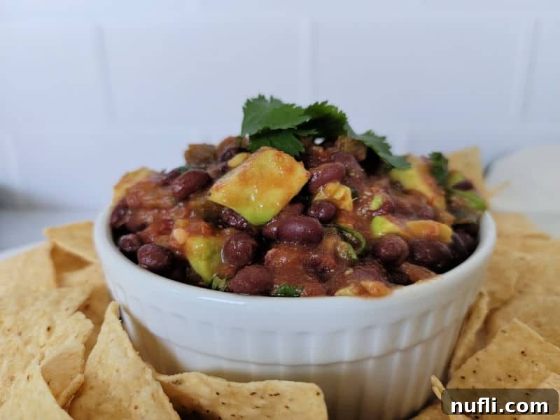 A close-up shot of a white bowl overflowing with freshly made black bean salsa, with crispy tortilla chips scattered around, inviting a dip.