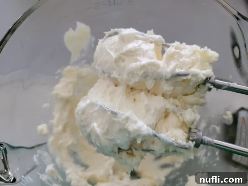 creamed cream cheese on hand mixer beaters in a glass bowl, ready for chocolate chip cream cheese ball mixture