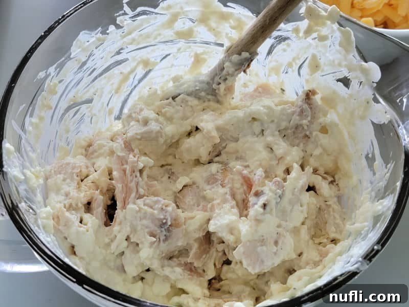 Shredded Chicken in a glass bowl being stirred with cream cheese mixture for Frank's Red Hot Buffalo Chicken Dip