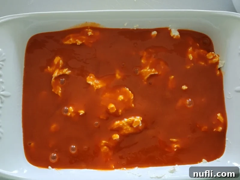 Franks Red Hot Buffalo Sauce spread over shredded chicken in a casserole dish for Buffalo Chicken Dip