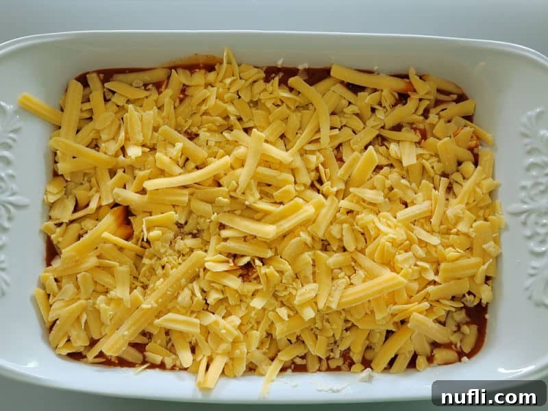 Shredded cheddar cheese spread over Franks Buffalo Sauce in a white casserole dish for Buffalo Chicken Dip 