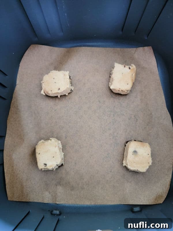 Air Fryer Cookie Delights 4 Cookie dough squares on parchment paper in an air fryer basket, perfectly spaced for baking.