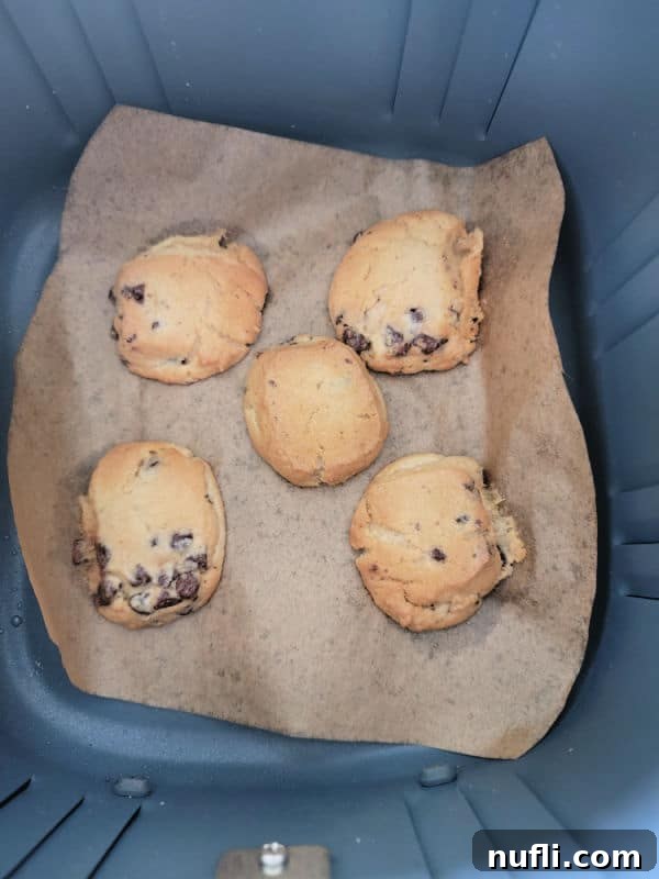 Air Fryer Cookie Delights 5 Freshly baked chocolate chip cookies on parchment paper in an air fryer basket, ready to be enjoyed.