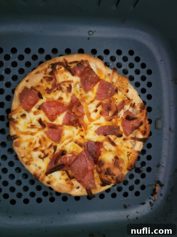 Air fried pepperoni pizza, golden and bubbly, inside an air fryer basket