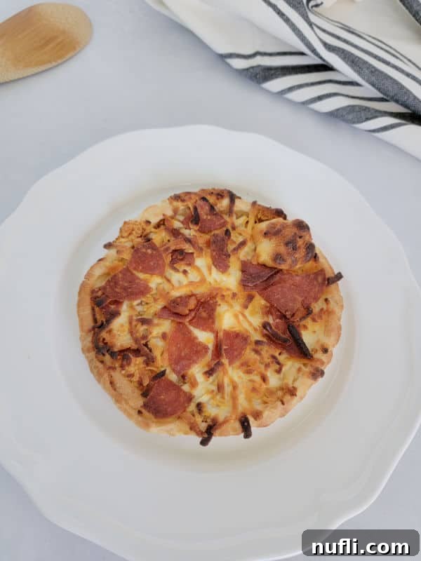 Air fried pepperoni pizza on a white plate next to a striped cloth napkin