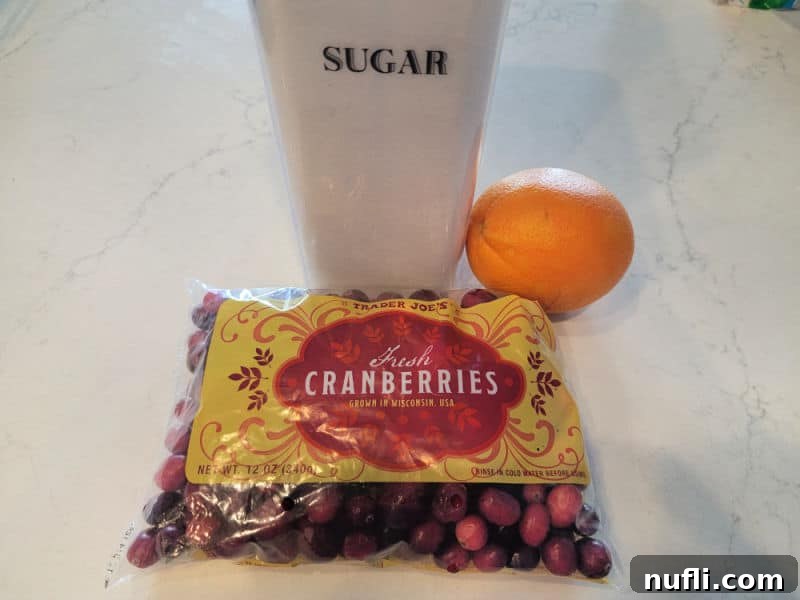 Cranberry relish ingredients, sugar, orange, cranberries on a white counter