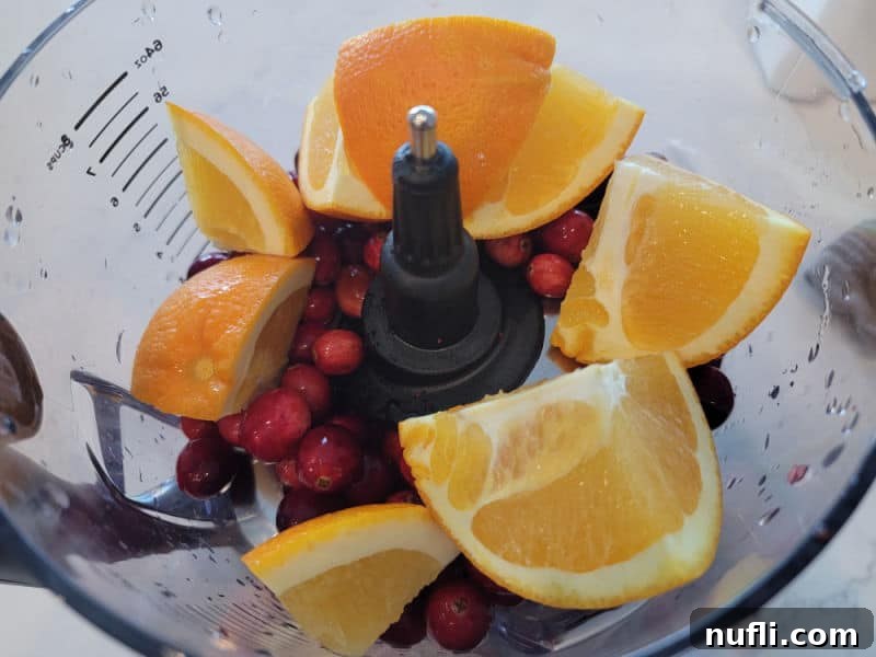 orange chunks, cranberries in the bowl of a food processor for cranberry relish