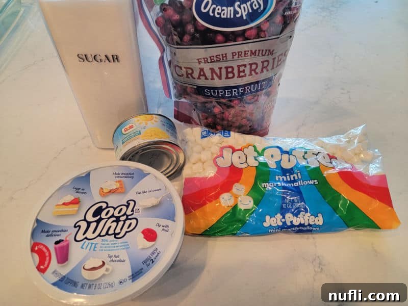 Quick and Easy Cranberry Fluff Salad 3 Cranberry Fluff Salad ingredients, sugar, fresh cranberries, cool whip, pineapple chunks, and mini marshmallows on a white counter