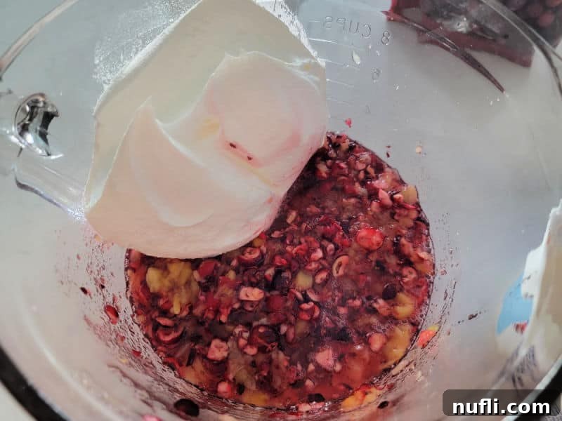 Quick and Easy Cranberry Fluff Salad 7 Cool whip in a glass bowl on pineapple pieces and shredded cranberries for cranberry salad