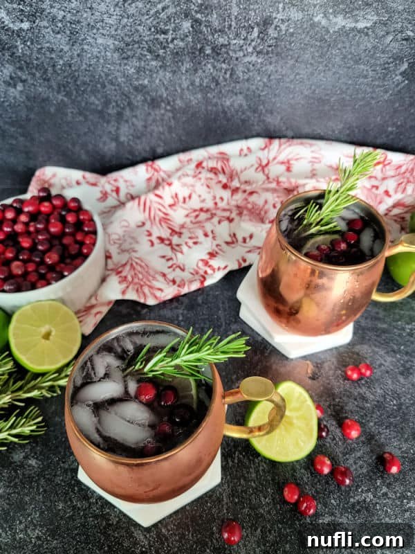 Cranberry Moscow Mule in a copper mug garnished with cranberries and rosemary next to a bowl of cranberries