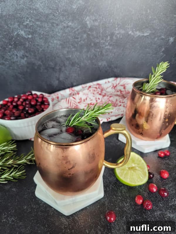 copper mule mugs with ice, liquid, and cranberries next to a bowl of cranberries and a white and red cloth napkin