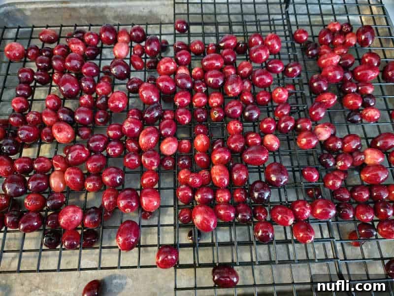 Simple syrup-coated cranberries drying on a wire rack, preparing for their sugar coating