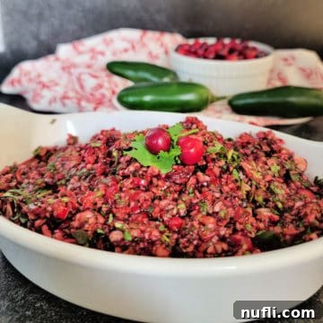 cranberry salsa in a white bowl with jalapenos and cranberries in the background