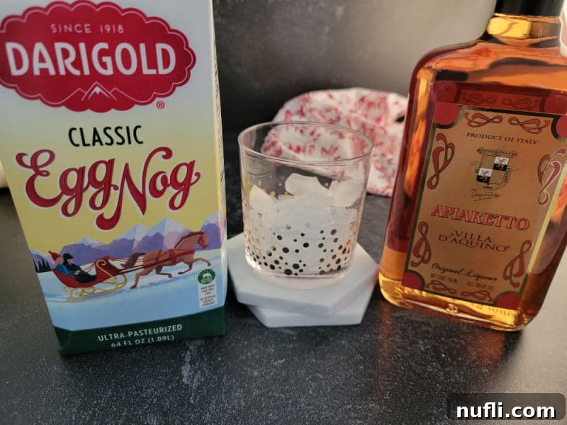 Simple Amaretto Eggnog Cocktail 3 Simple ingredients for an Amaretto Eggnog cocktail, featuring a bottle of Amaretto and classic eggnog, ready for mixing in a clear glass.