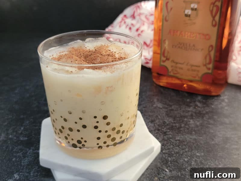 Simple Amaretto Eggnog Cocktail 4 A close-up shot of an Amaretto Eggnog cocktail in a glass, generously garnished with ground nutmeg, showcasing its inviting texture and festive look.