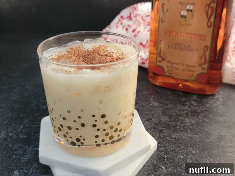 Simple Amaretto Eggnog Cocktail 8 Easy Amaretto Eggnog Cocktail garnished with ground nutmeg in a clear glass, presented elegantly on a festive surface.