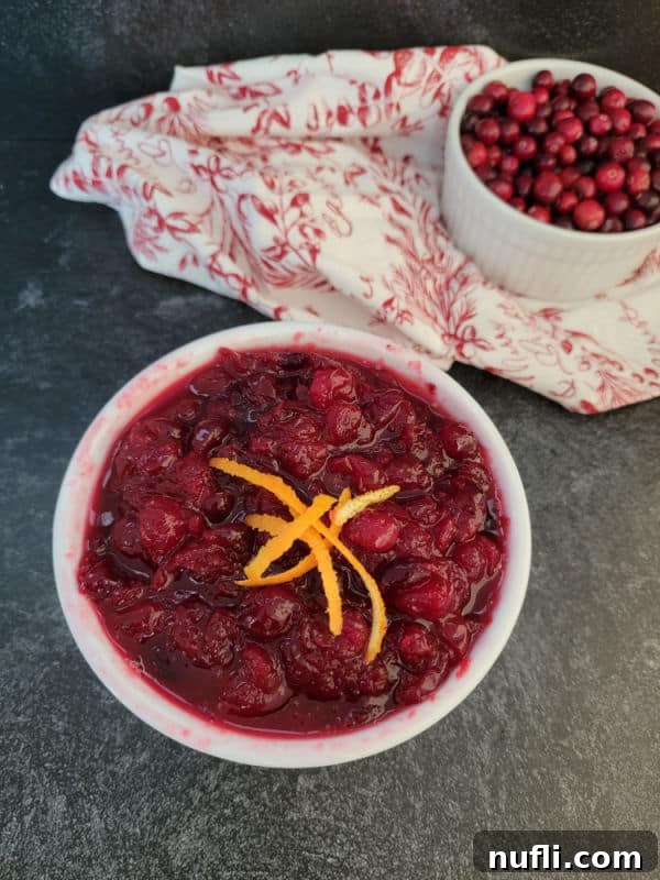 Homemade cranberry sauce in a white bowl with orange strips next to a bowl of fresh cranberries
