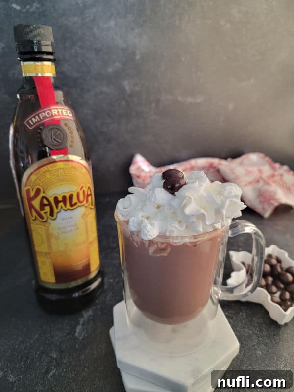 Decadent Kahlua Hot Chocolate 5 A close-up of a glass mug filled with Kahlúa Hot Chocolate, adorned with whipped cream and chocolate shavings, beside a Kahlúa bottle.