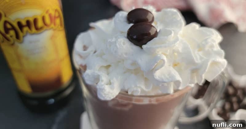 Decadent Kahlua Hot Chocolate 7 A charming close-up of Kahlúa Hot Chocolate in a glass mug, featuring a generous swirl of whipped cream, beside a bottle of Kahlúa, all on a rustic wooden surface.