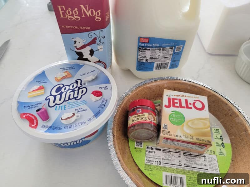 Eggnog Pie ingredients cool whip, egg nog, milk, vanilla pudding mix, nutmeg, and a graham cracker crust on a white counter