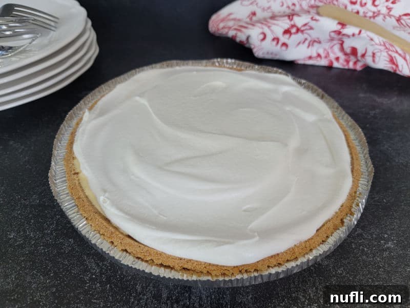 No bake eggnog pie topped with cool whip on a dark counter next to plates and forks