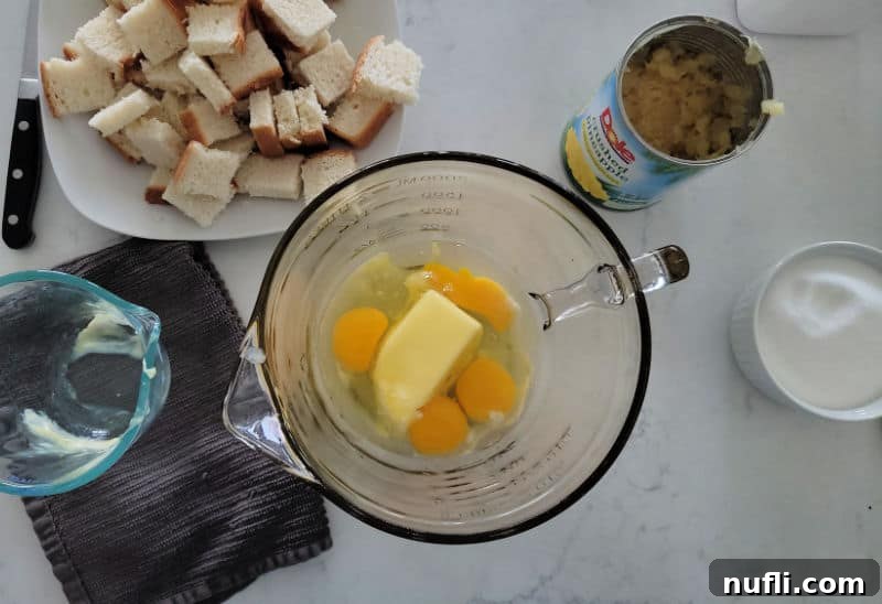 Effortless 5 Ingredient Pineapple Stuffing 4 butter and eggs in a glass mixing bowl next to cut up bread pieces, and pineapple in a can