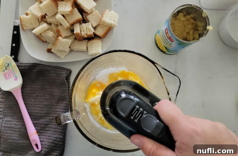 Effortless 5 Ingredient Pineapple Stuffing 5 hand mixer in a bowl next to bread pieces and pineapple in a can