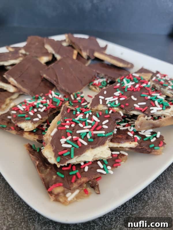 Irresistible 4 Ingredient Christmas Crack 12 Christmas Crack Saltine Cracker Toffee on a white plate covered in holiday sprinkles