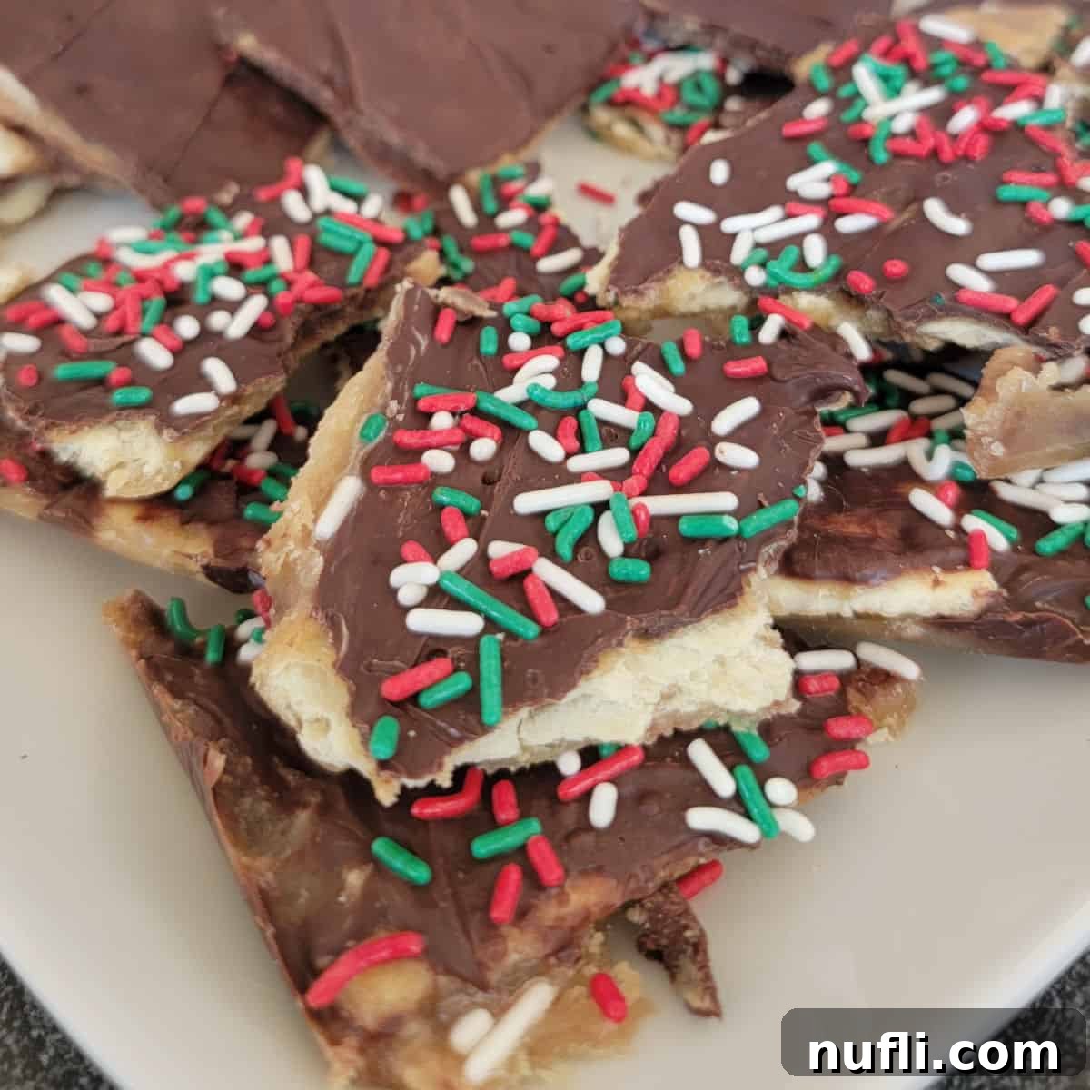 Irresistible 4 Ingredient Christmas Crack 14 Pieces of Saltine Toffee with sprinkles on them on a white plate