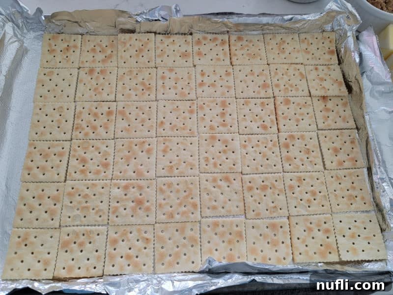 Irresistible 4 Ingredient Christmas Crack 5 Saltine crackers spread on an aluminum foil lined baking dish for Christmas Crack Saltine Toffee
