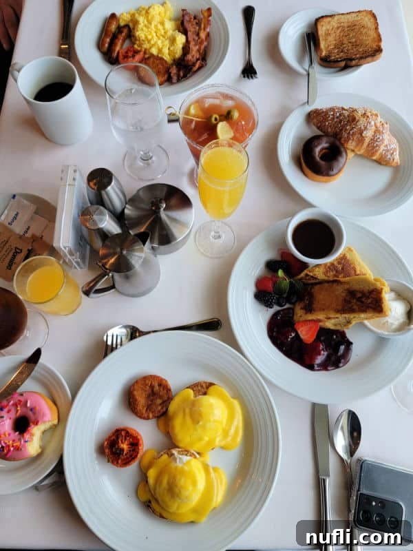 breakfast spread over a white table cloth including eggs benedict, French toast, a donut, croissant, Bloody Mary and Orange Juice