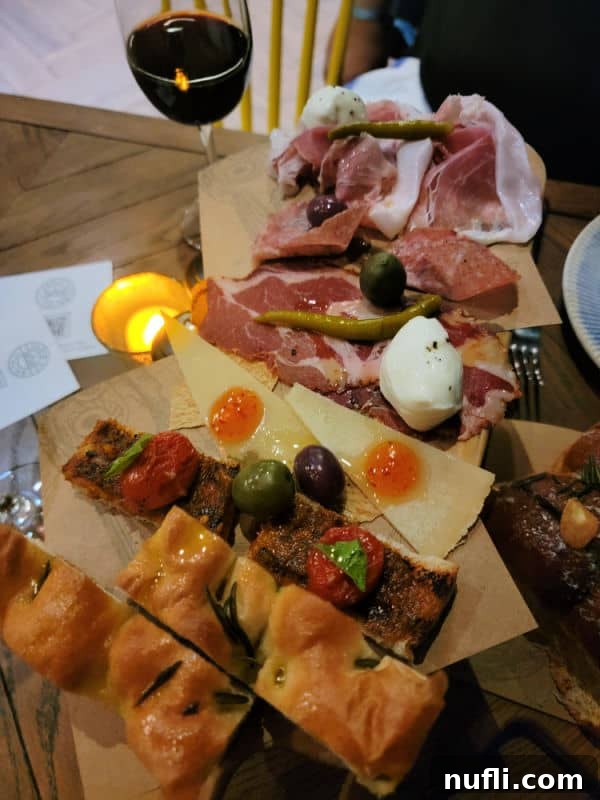 Glass of wine next to an antipasto platter with bread and meats. 