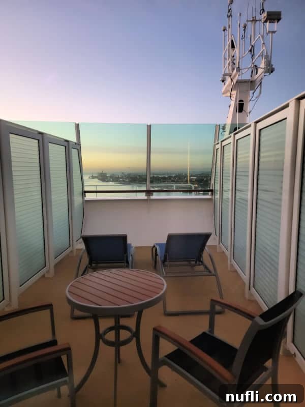 table and chairs near lounge chairs with the ocean and a city in the background