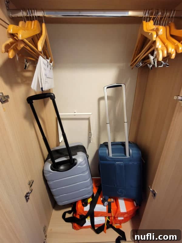 An open closet revealing two suitcases, two life jackets, and a selection of hangers, efficiently organized within a cruise ship stateroom for essential storage.