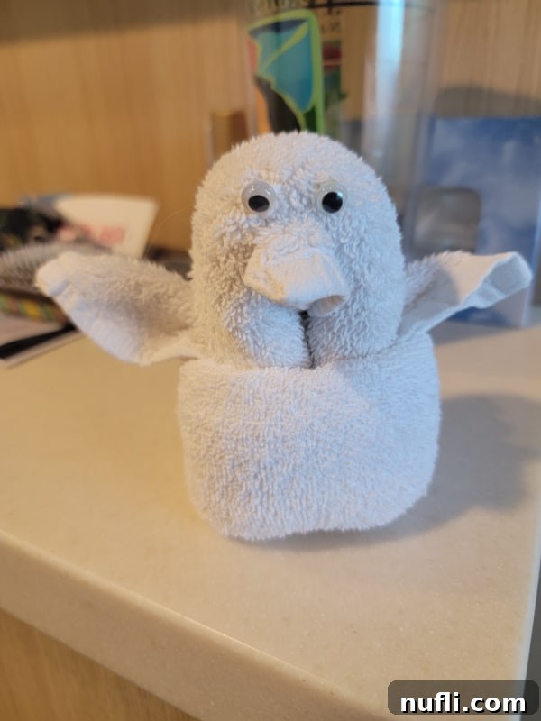 A charming towel animal shaped like a penguin, complete with adorable eyes, resting on a bed in a cruise ship stateroom.